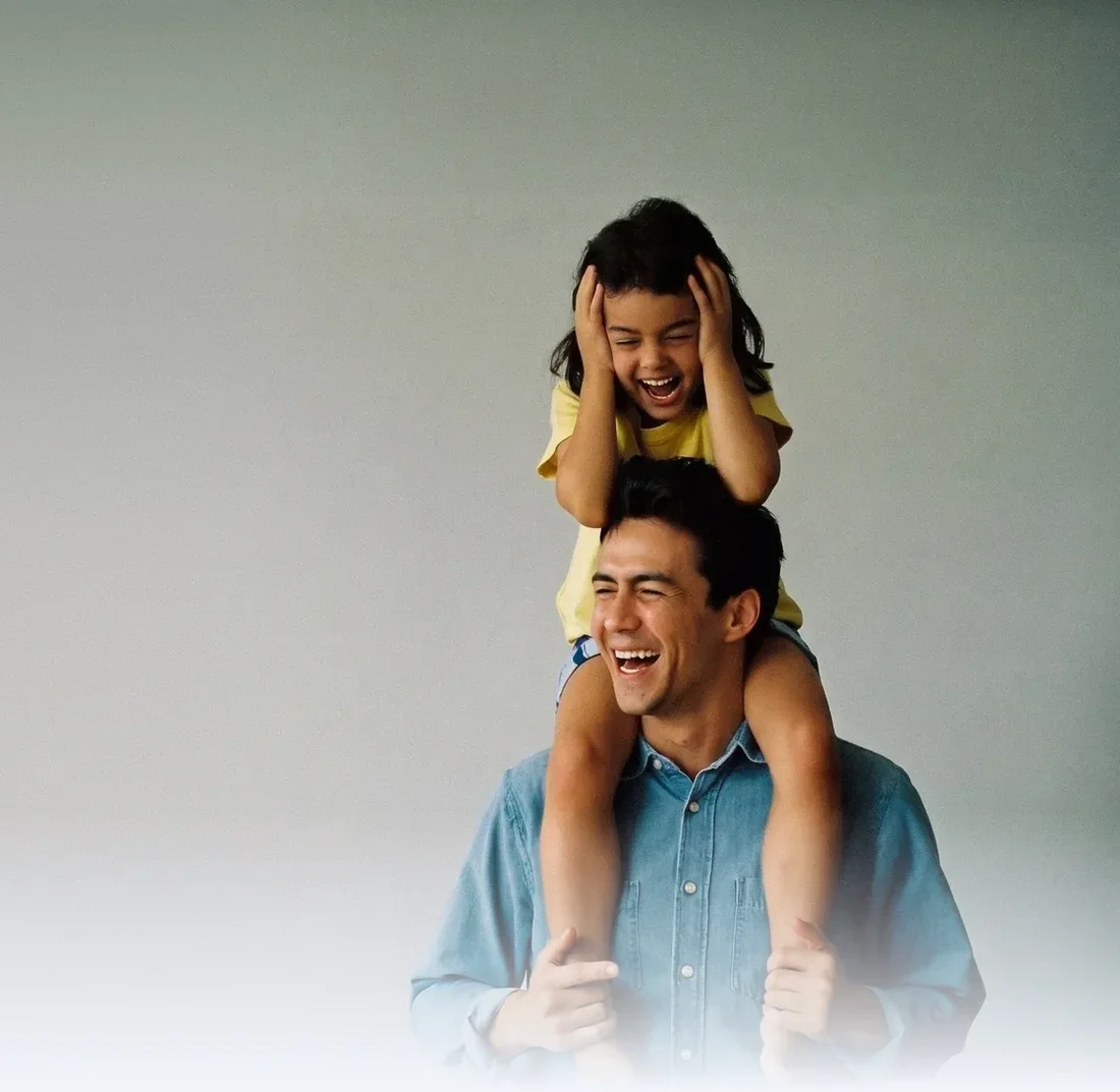 Padre riendo mientras carga a su hija en hombros frente a un fondo liso de estudio