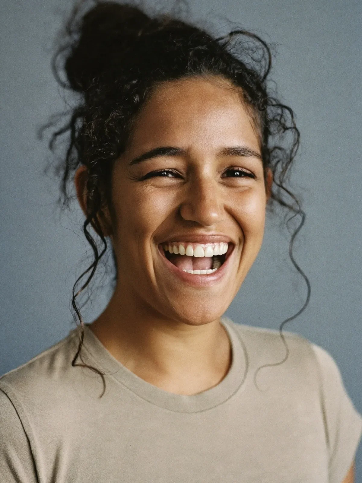 Young woman laughing, photographed against a plain backdrop