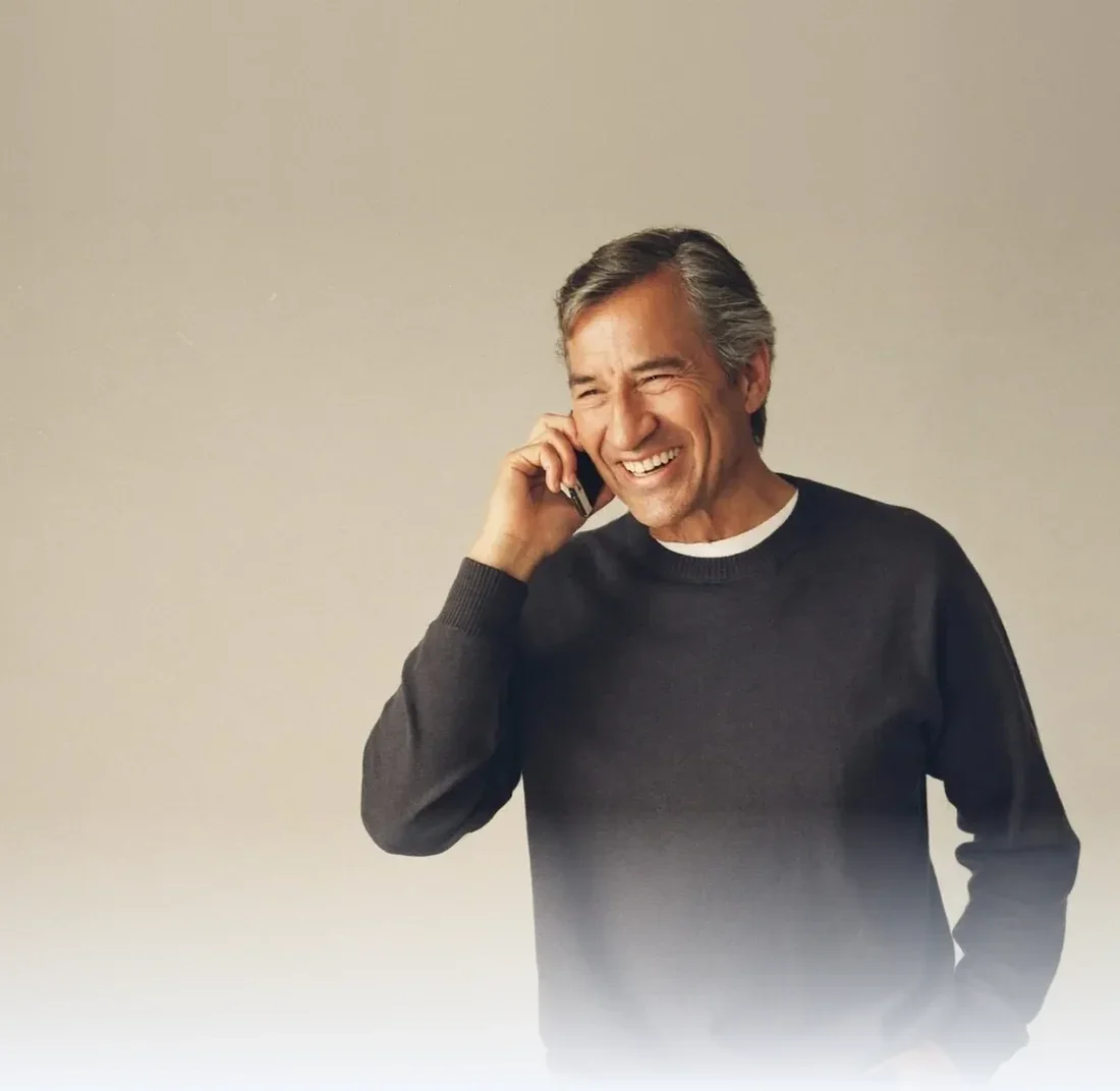 Man smiling while talking on a mobile phone against a plain studio backdrop