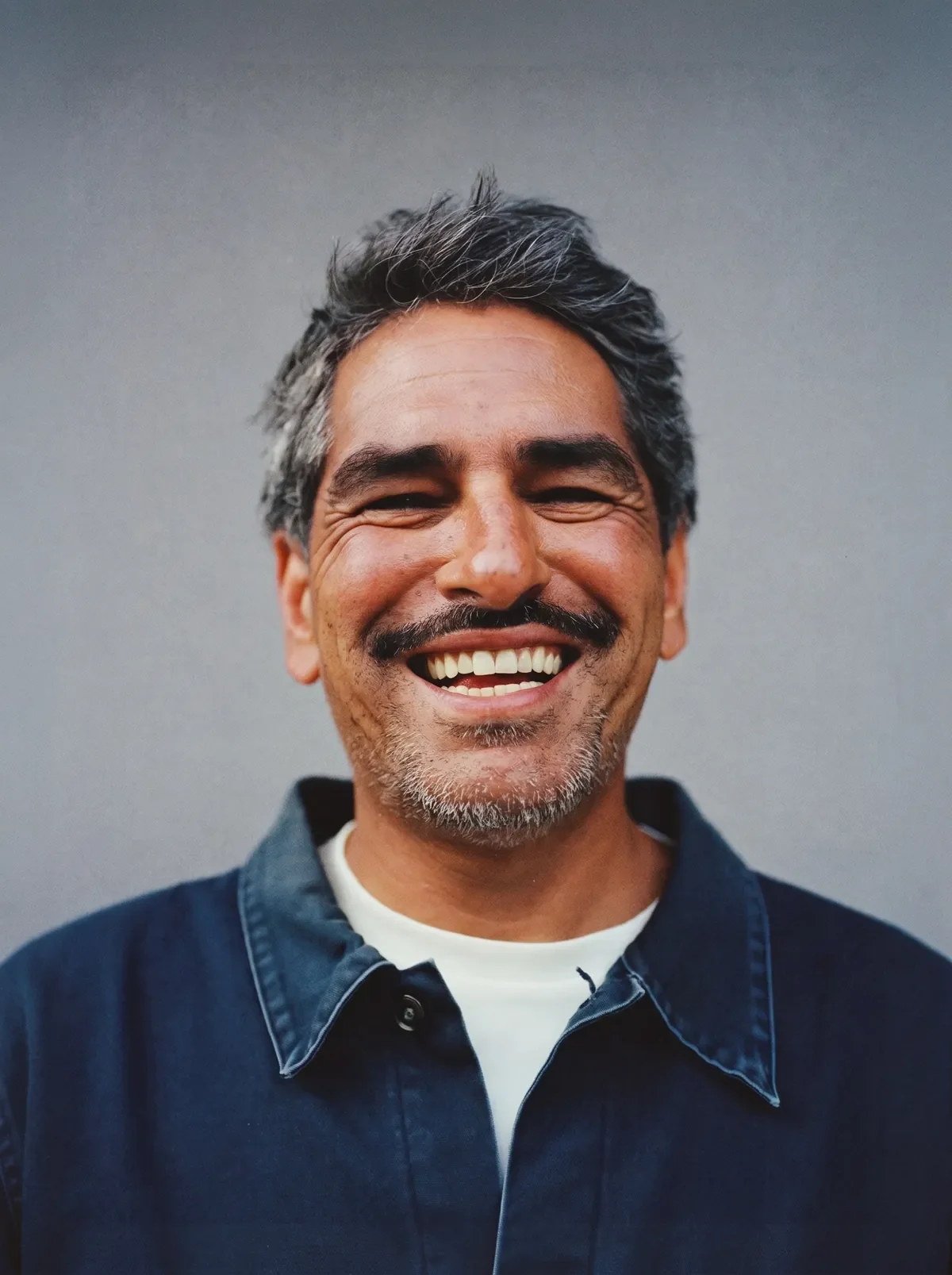 Older man smiling, photographed against a plain backdrop