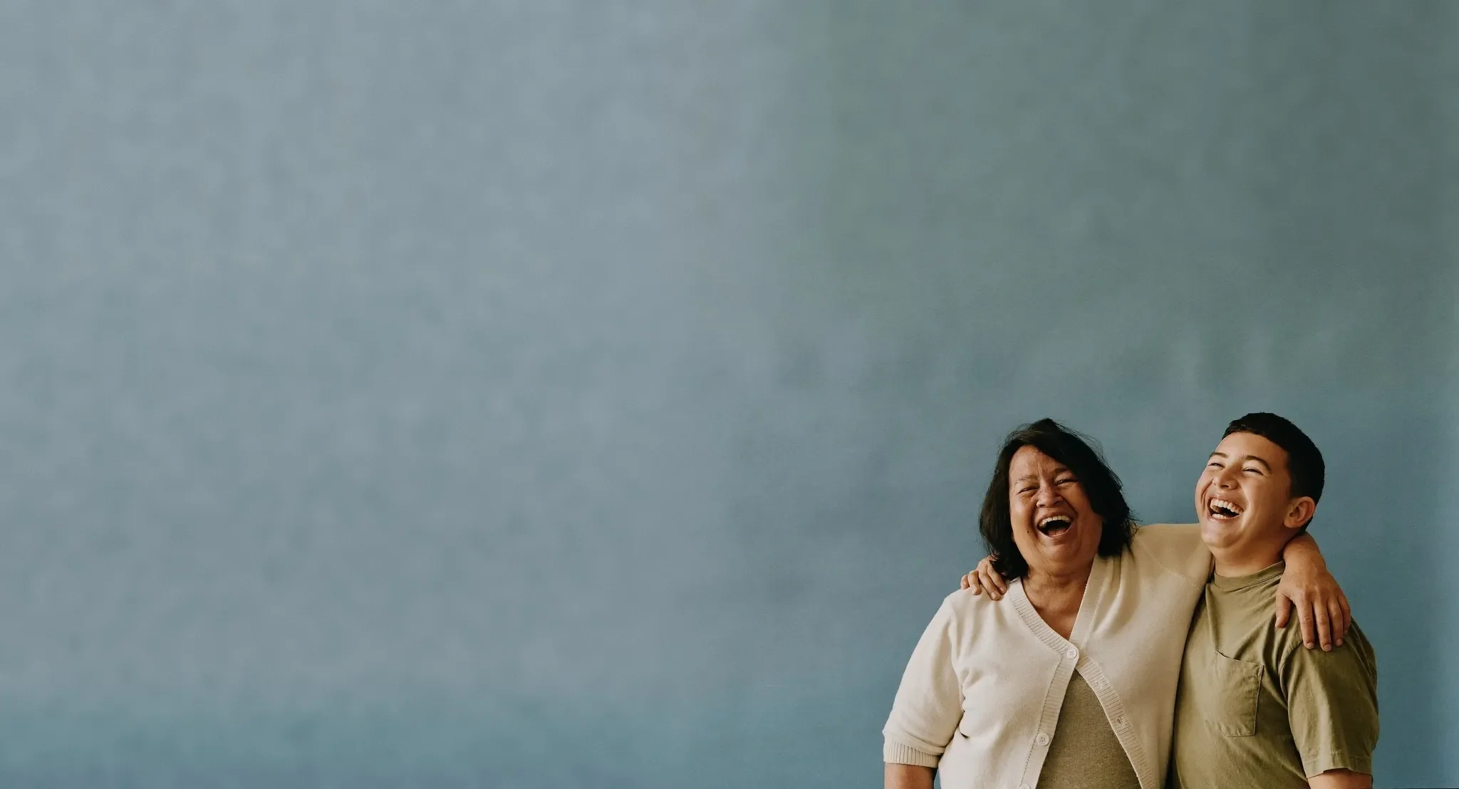Grandmother and teenage grandson laughing together against a plain studio backdrop
