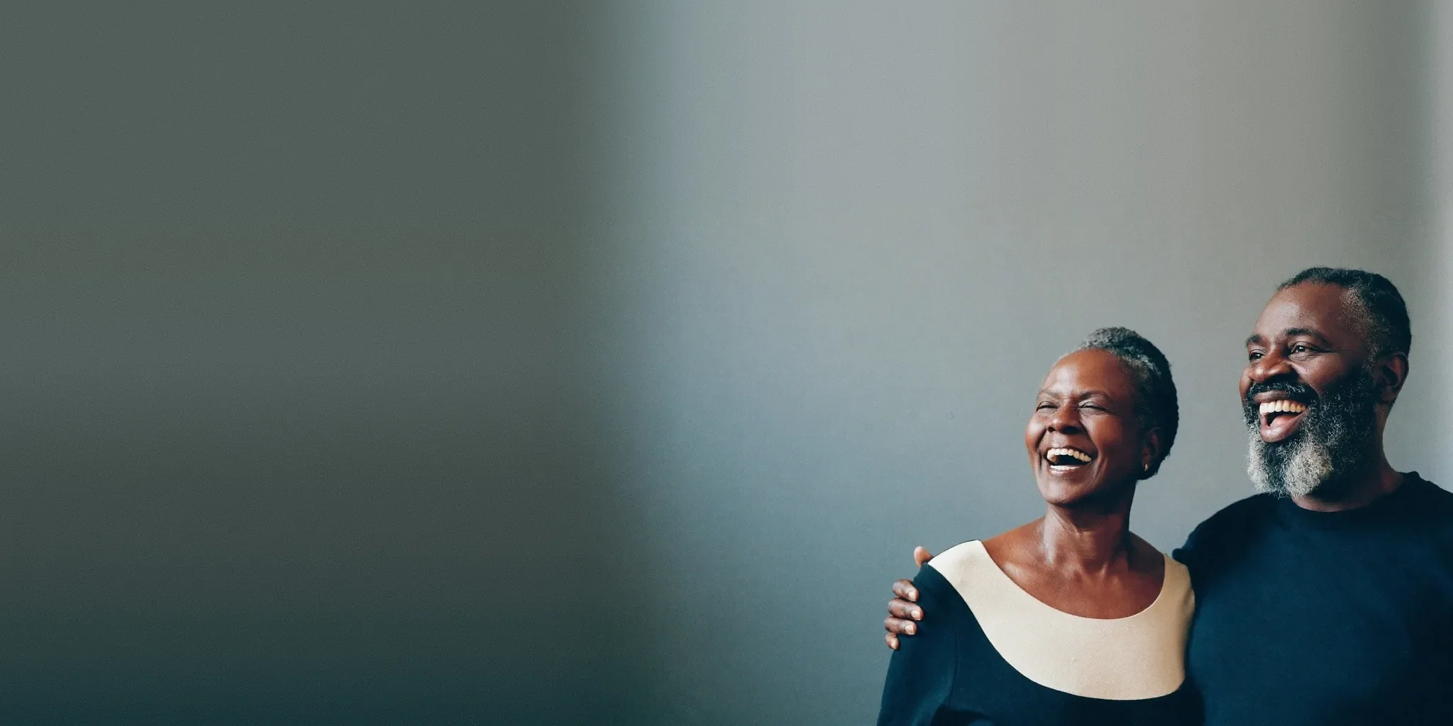 Couple laughing together against a plain studio backdrop