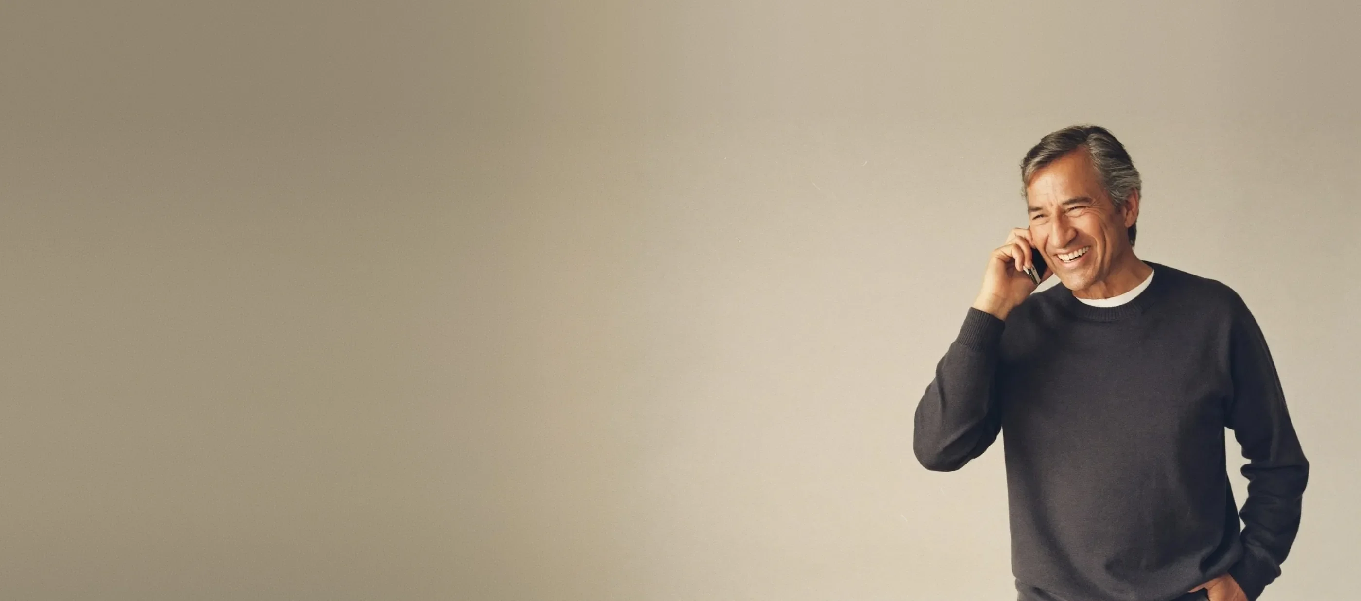 Man smiling while talking on a mobile phone against a plain studio backdrop