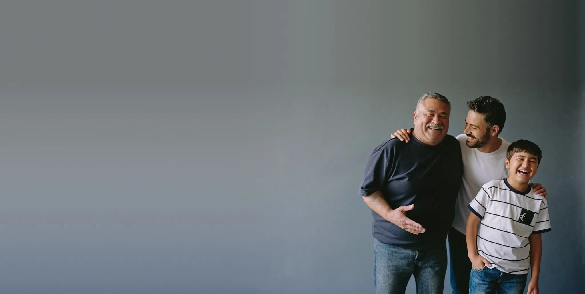 Three generations of a family laughing together against a plain studio backdrop