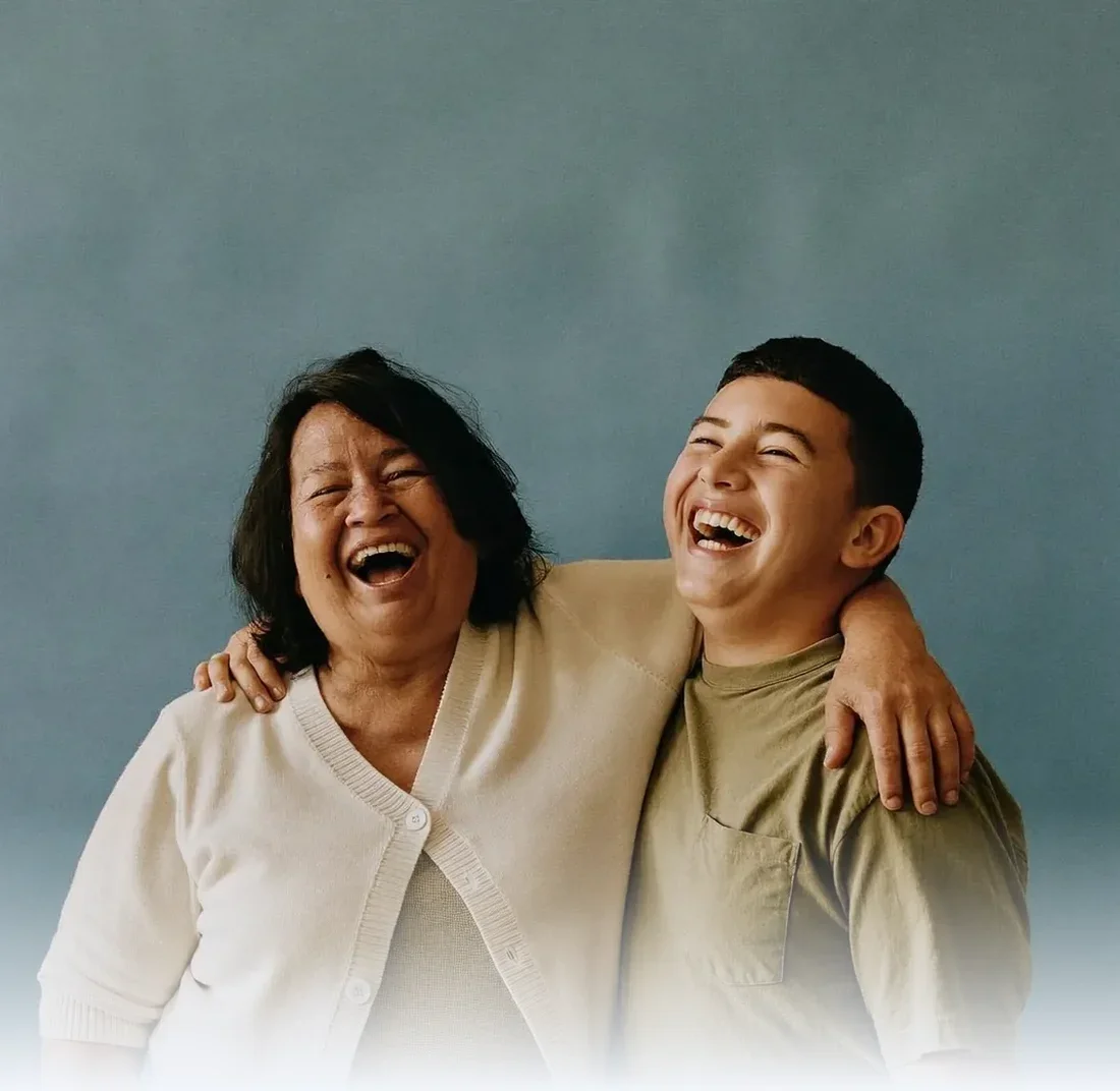 Grandmother and teenage grandson laughing together against a plain studio backdrop