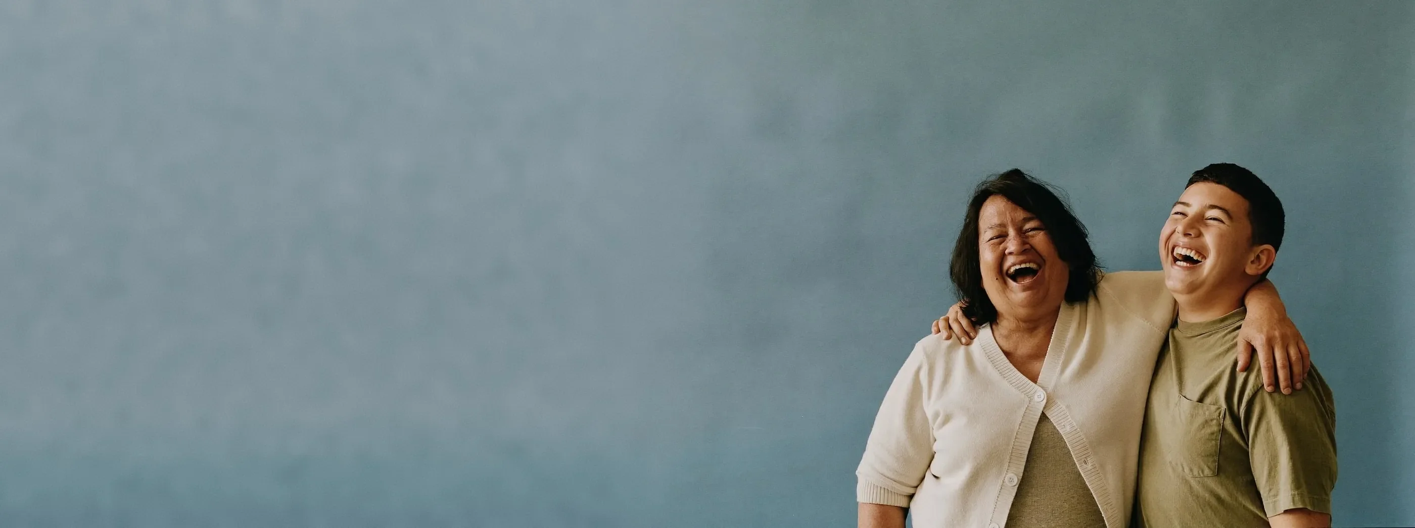Grandmother and teenage grandson laughing together against a plain studio backdrop