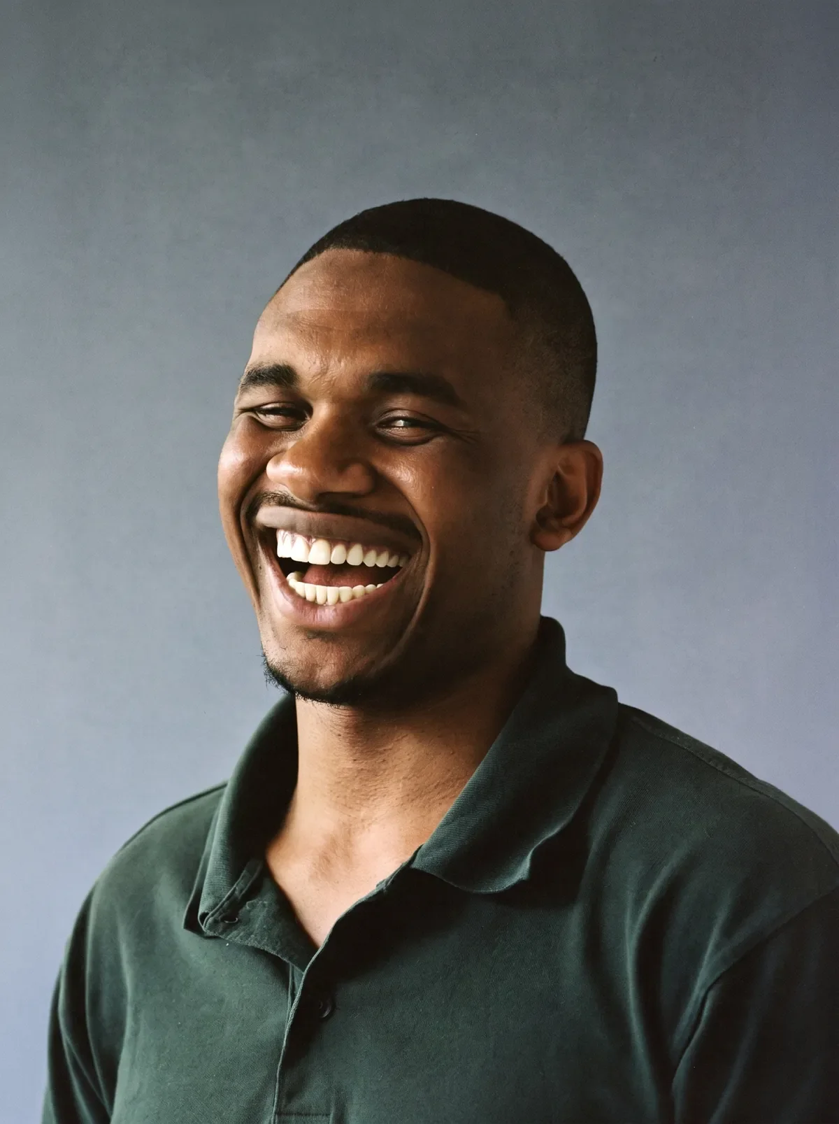 Young man grinning, photographed against a plain backdrop