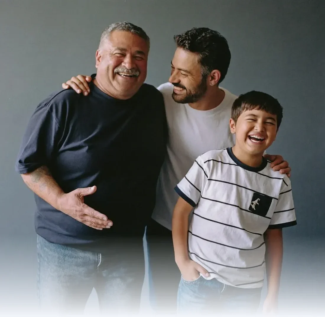 Three generations of a family laughing together against a plain studio backdrop